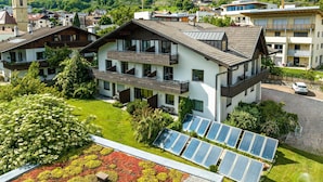 Um edifício moderno com várias varandas, painéis solares e um jardim exuberante.