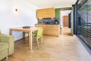 A modern kitchen with wooden cabinets, a dining table with chairs, and a view through a glass door.