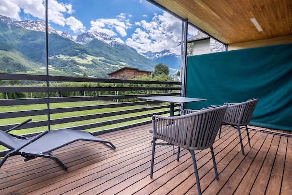 A wooden deck with a table and chairs, overlooking a mountainous landscape.