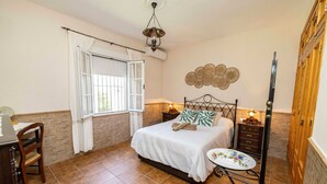 Une chambre à coucher comprenant un lit, une table de chevet, une chaise et une petite table recouverte d’une nappe à motifs floraux.