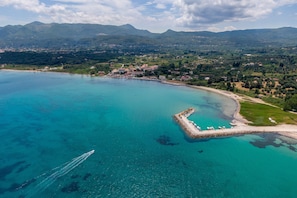 An aerial view of a coastal town with a clear turquoise sea, a small peninsula with a pier, and surrounding green hills. - Studio Apartment 'Standard' with Sea View, Wi-Fi and Air Conditioning (Corfu)