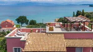 A rooftop terrace with a checkered sunshade, a seating area with outdoor furniture, and a view of the sea and distant mountains.
