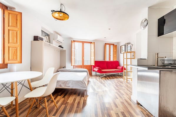 A modern kitchen with a dining area, a red sofa, and a bed.