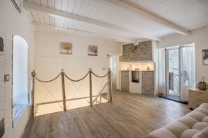 Une pièce spacieuse avec un plafond haut, un escalier en bois, une cheminée et une vue sur l’extérieur.