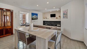 Una sala de estar moderna con chimenea, un comedor con mesa y sillas de madera, y un televisor montado en la pared.