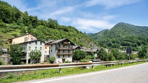 Una carretera de montaña con edificios a la izquierda, una barandilla y una montaña al fondo.