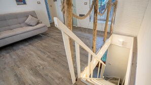 Una habitación con piso de madera, un sofá blanco y una escalera con barandilla de cuerda.