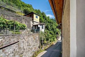 Une route étroite, bordée d’un côté par un mur de pierres et de l’autre par un bâtiment dont le toit est jaune.