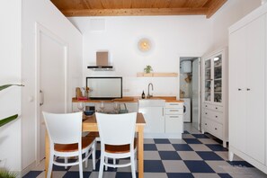 Une cuisine de taille réduite avec des meubles blancs, une table à manger en bois et un sol à carreaux.
