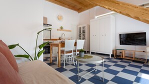 A room with a checkered floor, a dining area with chairs and a table, a TV mounted on the wall, and a wooden ceiling.