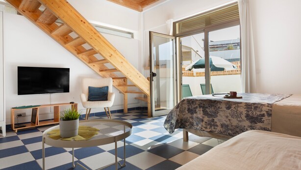 A room with a checkered floor, a bed, a chair, a TV, a staircase, and a sliding glass door.