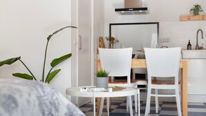 A modern kitchen with white cabinetry, a wooden countertop, and a built-in stove. There are two white chairs, a small round table, and a potted plant.
