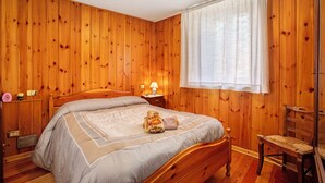Una stanza con rivestimenti in legno, un letto, una sedia, un comodino e una finestra con tende.