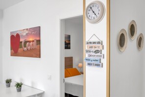 Une pièce comprenant un lit, une horloge murale, une affiche motivante et une petite table sur laquelle sont posées des plantes en pot.