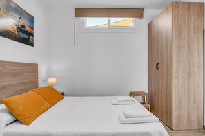 Une chambre à coucher avec un lit, une table de chevet, une armoire en bois, une fenêtre et un tableau accroché au mur.