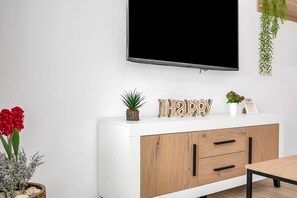 A white cabinet with wooden handles, a television mounted on the wall, and decorative items including a 'Happy' sign and small potted plants. - Holiday Home 'Casa Sol De Conil' with Private Pool, Private Terrace and Wi-Fi (Conil de la Frontera)