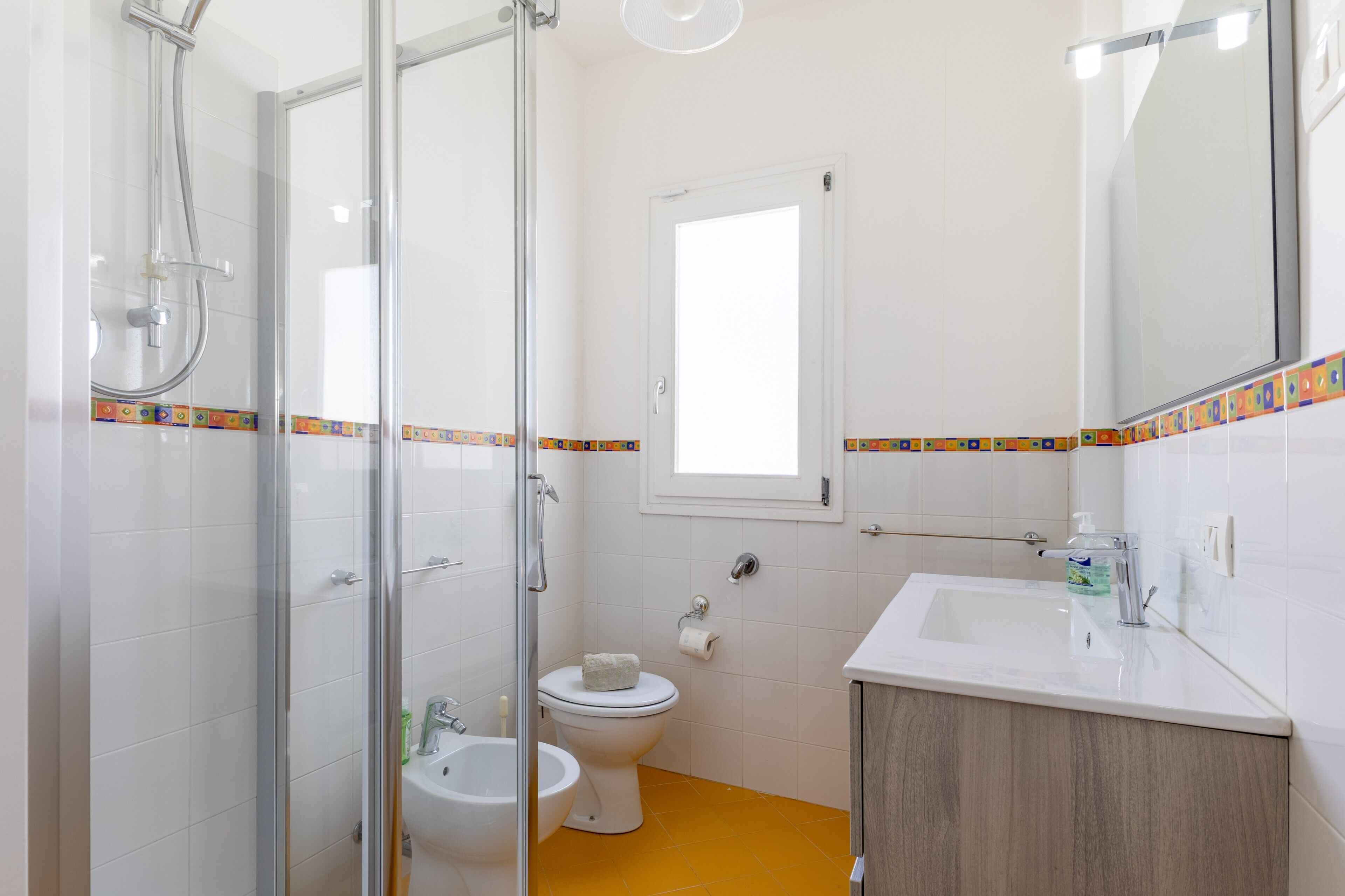 A bathroom with a glass shower enclosure, a toilet, a bidet, and a sink with a mirror.