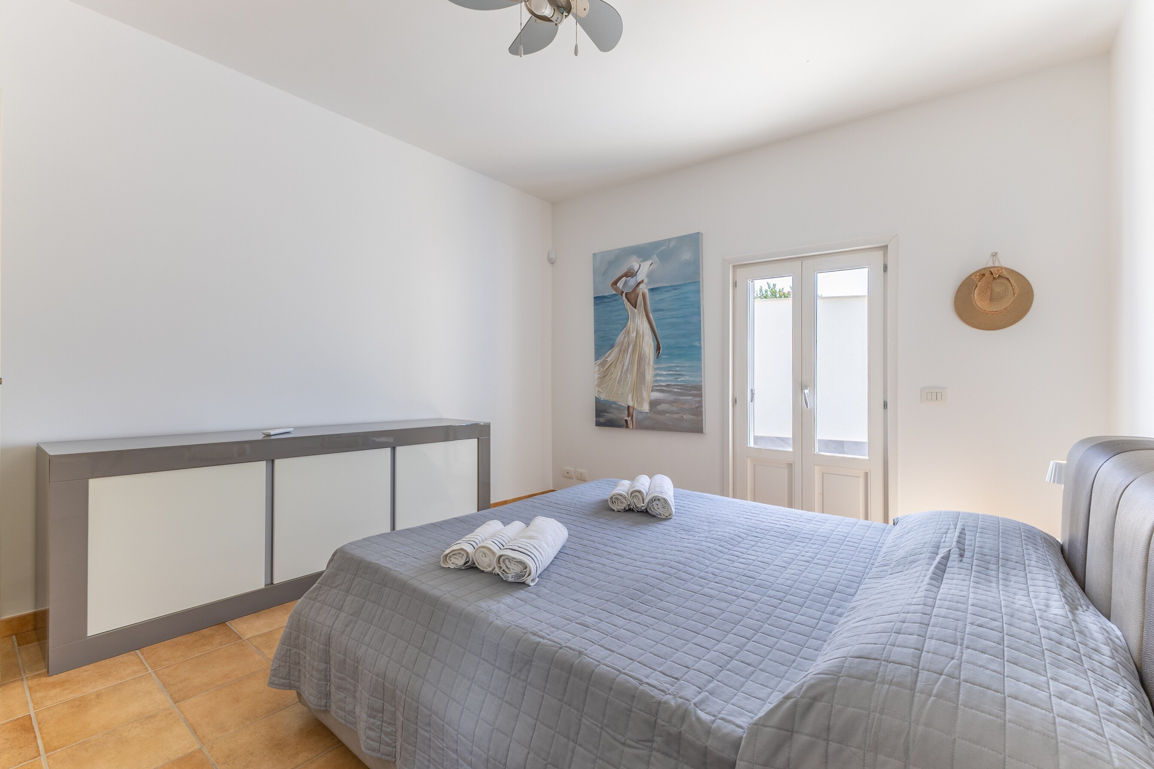Een slaapkamer met een bed, nachtkastje, schilderij en een deur.