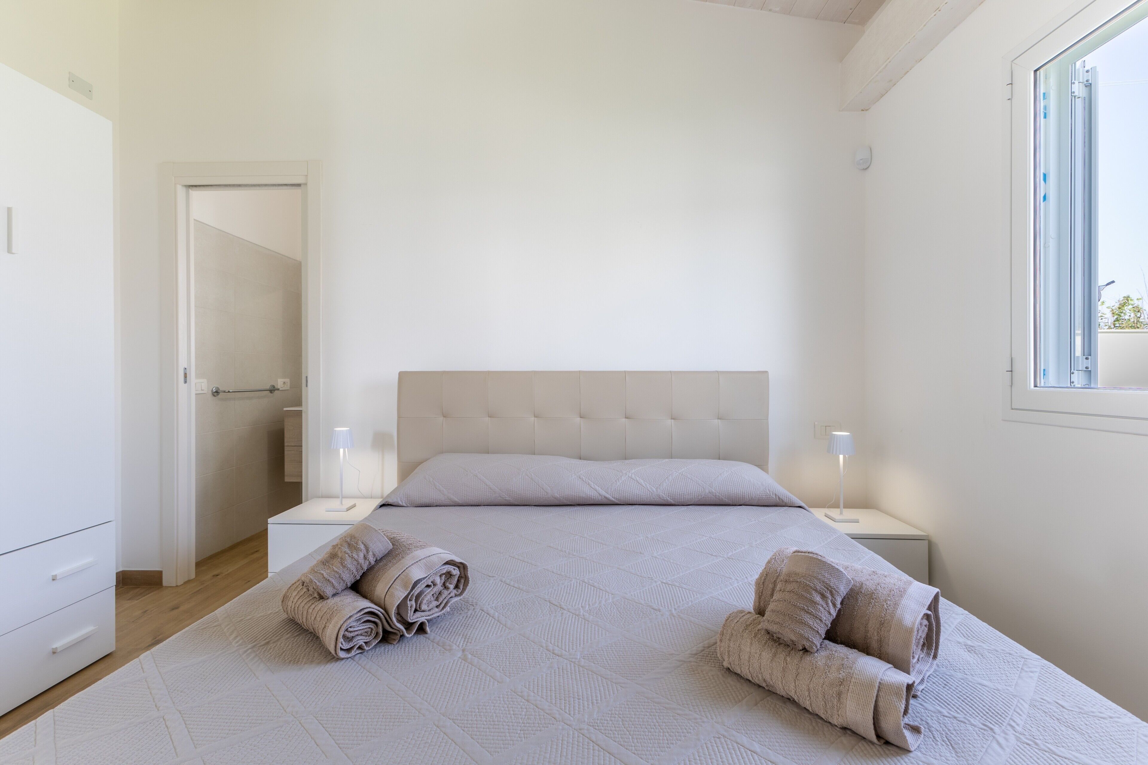 A bedroom with a large bed, two bedside tables with lamps, a wardrobe, and a window.