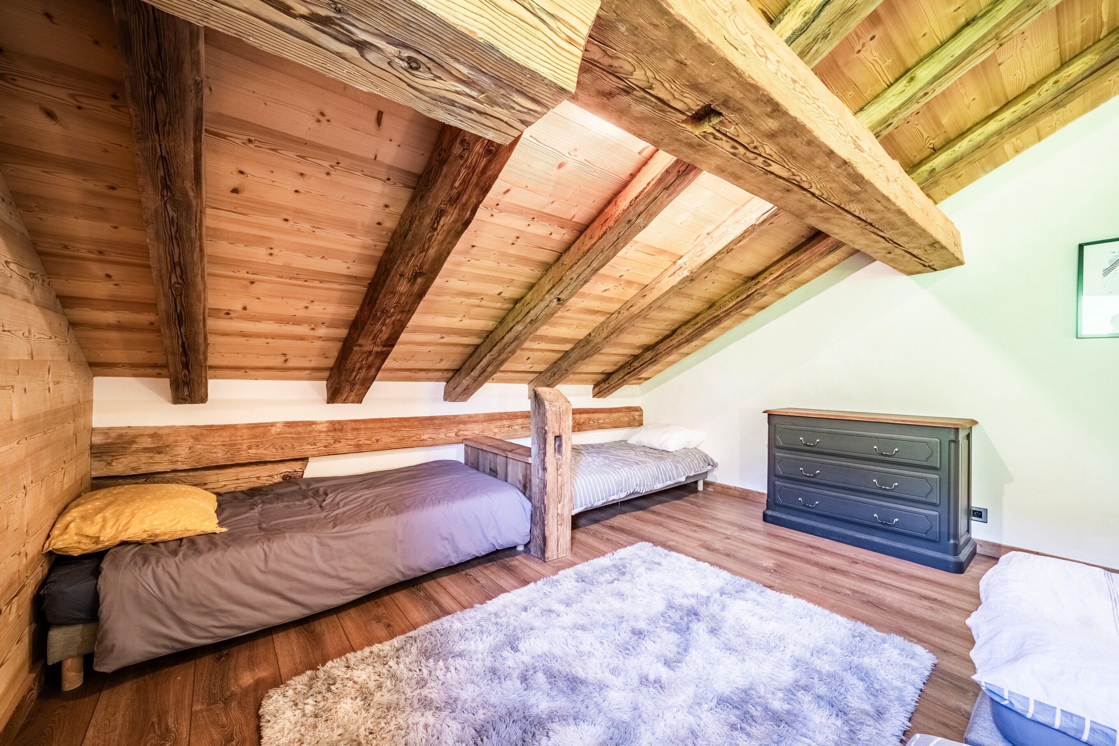 A loft bedroom with exposed wooden beams, a bunk bed, a dresser, and a fluffy rug.