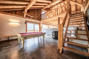 Un intérieur en bois avec une table de billard, un escalier et une vue sur l’extérieur.