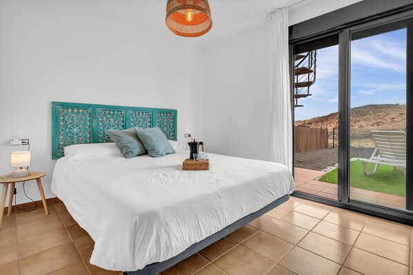 Une chambre à coucher avec un grand lit, une table de chevet, une lampe, une fenêtre donnant sur une colline et un luminaire au plafond.