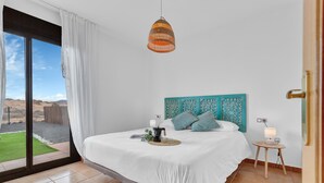 Quarto com cama, mesa de cabeceira, luminária pendente e vista através de uma janela grande.