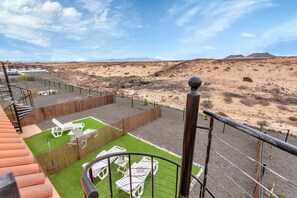 Een balkon met uitzicht op een woestijnlandschap, een omheind gazon met witte ligstoelen, en een trap.