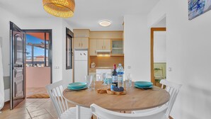 Cozinha moderna com armários brancos, mesa de jantar de madeira e vista para o exterior.