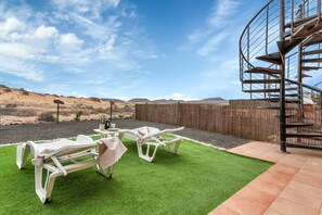 Un patio con dos sillones blancos, una escalera espiral y vistas al paisaje desértico.