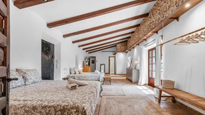 Un dormitorio con dos camas, vigas de madera, una pared de piedra y vistas a un jardín.