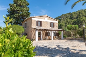 A stone house with a tiled roof, a covered porch, and a stone courtyard.