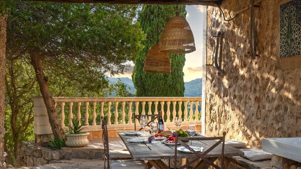 Un área de comedor al aire libre con una mesa de piedra, sillas y lámparas de mimbre colgantes.
