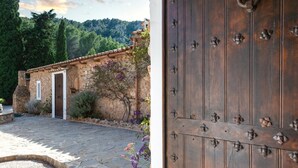 Un edificio rústico de piedra con puerta de madera, un patio empedrado y montañas al fondo.