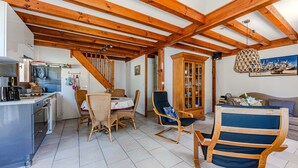 A spacious living area with exposed wooden beams, a dining table with chairs, a kitchen area, and a wooden cabinet. - Holiday Home 'Maison Océlandes' with Shared Pool, Private Terrace and Wi-Fi (Saint-Julien-en-Born)