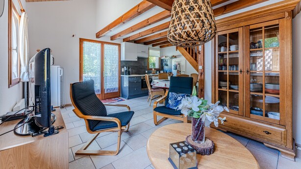 A spacious living room with wooden beams, a television, a dining area, and a kitchen in the background. - Holiday Home 'Maison Océlandes' with Shared Pool, Private Terrace and Wi-Fi (Saint-Julien-en-Born)