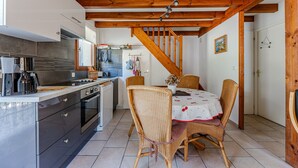 A kitchen with modern appliances, a dining area with wicker chairs, and a wooden staircase. - Holiday Home 'Maison Océlandes' with Shared Pool, Private Terrace and Wi-Fi (Saint-Julien-en-Born)