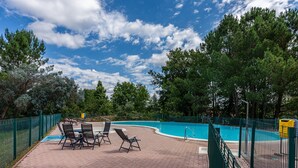 A swimming pool with a green fence, lounge chairs, and trees in the background. - Holiday Home 'Maison Océlandes' with Shared Pool, Private Terrace and Wi-Fi (Saint-Julien-en-Born)