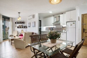 Une cuisine moderne avec des meubles blancs, un réfrigérateur et un coin repas comprenant une table et des chaises en verre.