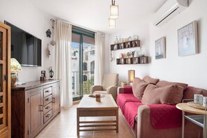 A living room with a sofa, a coffee table, a TV, a cabinet, and a balcony with a view. - Apartment 'Bella Vistas' with Shared Pool, Wi-Fi and Air Conditioning (Zahara de los Atunes)