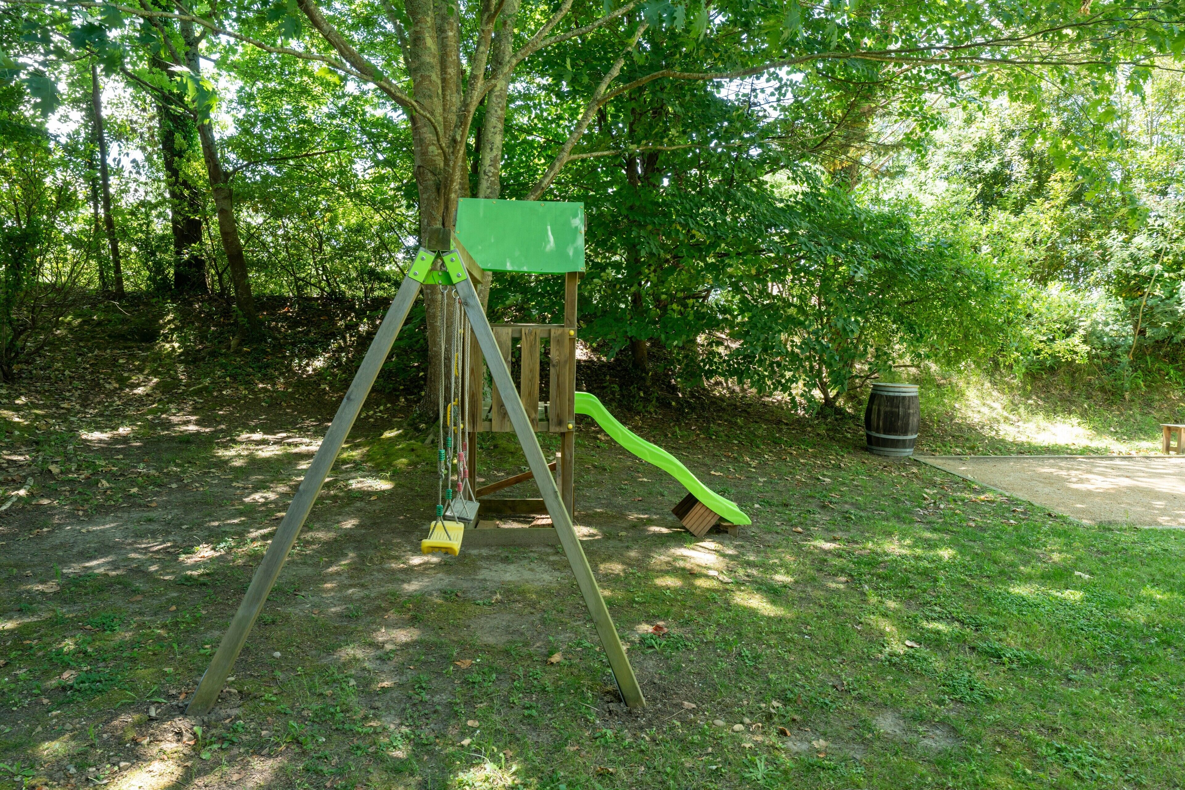 Un'area giochi con altalene, scivolo e struttura verdeggiante in un parco alberato.