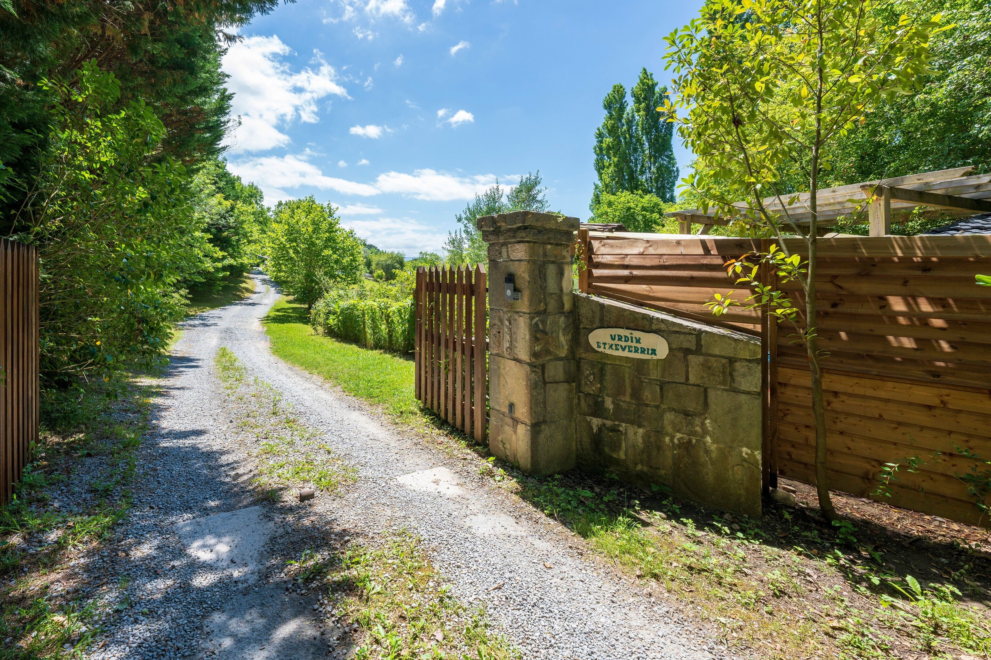 A gravel path leading to a wooden gate with a stone wall and a sign.