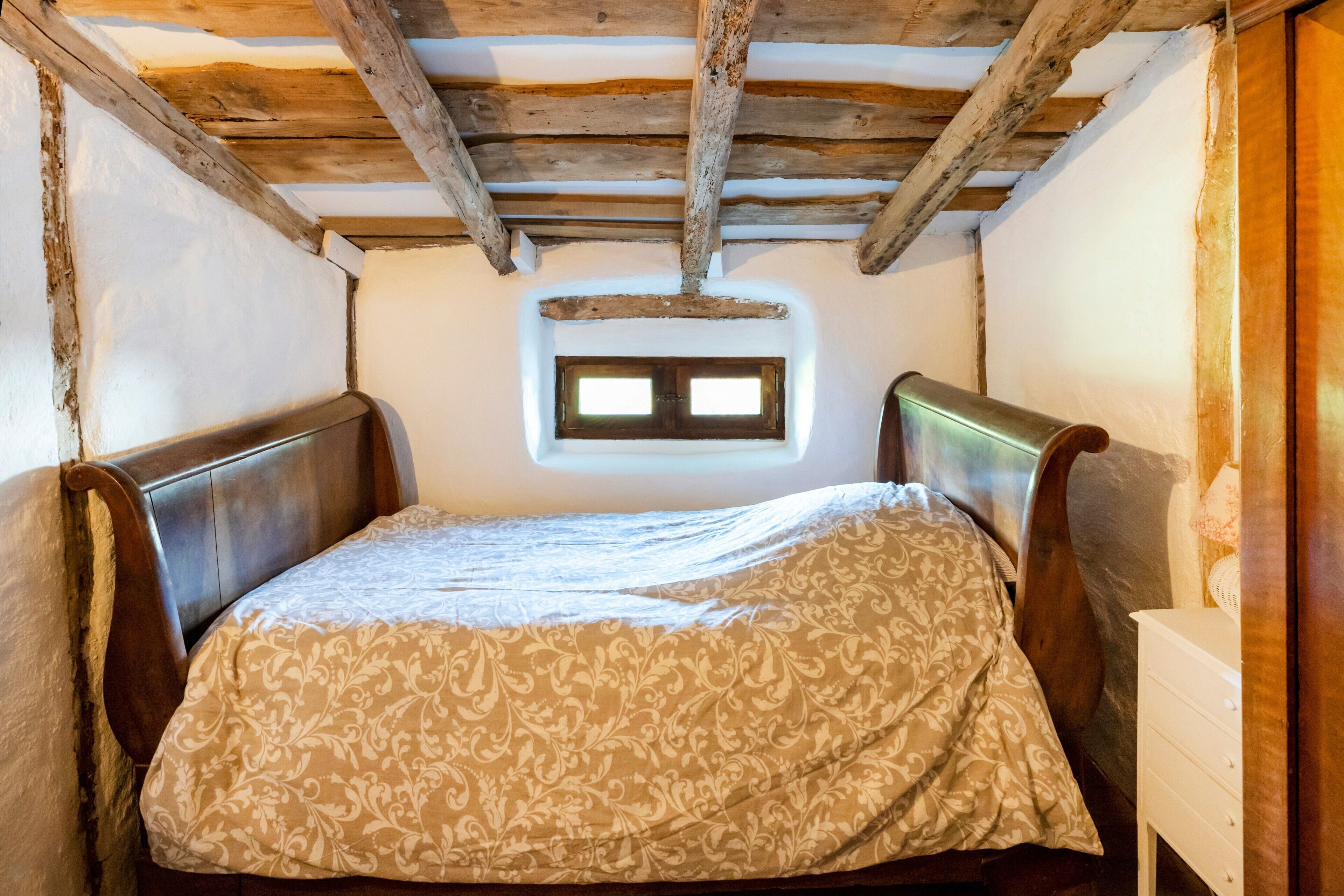 A small, rustic room with a wooden ceiling, a single bed with a patterned bedspread, and a small window.