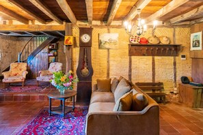 Un interior rústico con una escalera de madera, un reloj grande, un sofá y un tapiz estampado.
