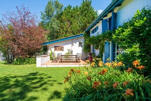 Una casa con patio, banco y jardín lleno de flores.