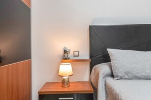 En pænt redt seng med en grå pude, en sengetavle med en lampe og en lille hylde med en figur og en billedramme.