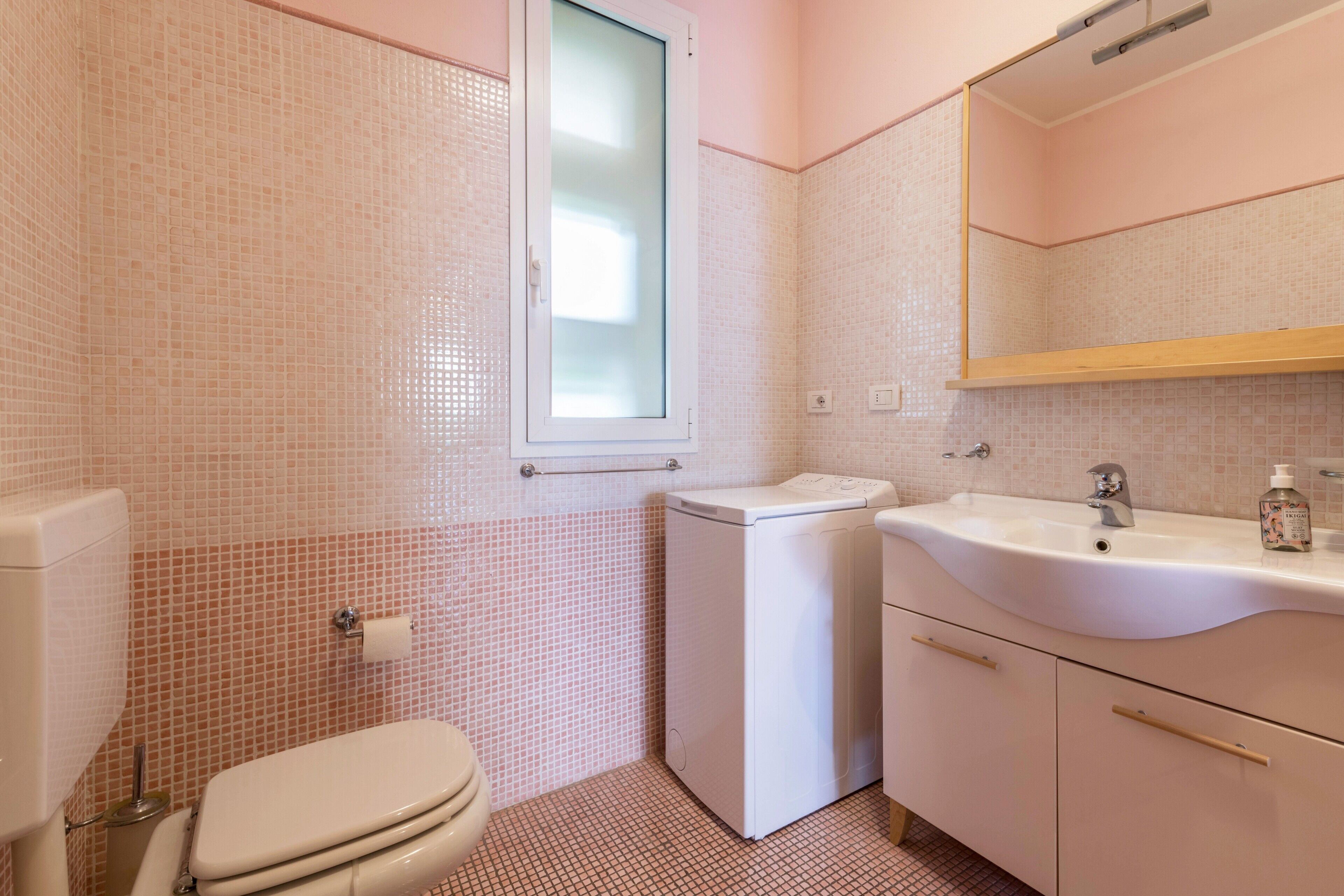 A bathroom with a toilet, washing machine, sink, and mirror.