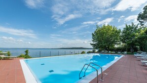 A swimming pool with a view of the sea, surrounded by a tiled deck and lounge chairs.