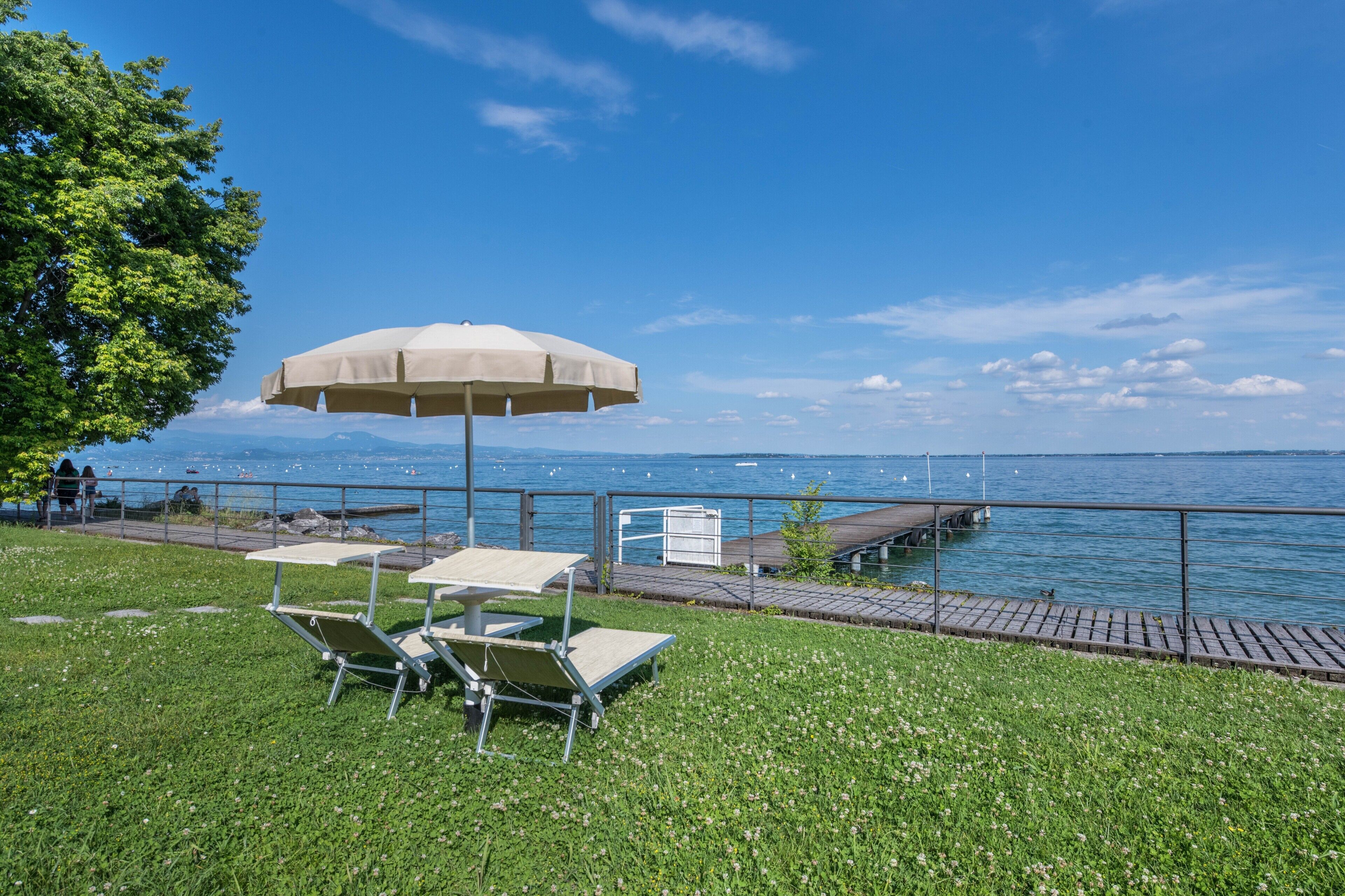 A grassy outdoor area with a table and chairs under a canopy, overlooking a body of water and a dock.