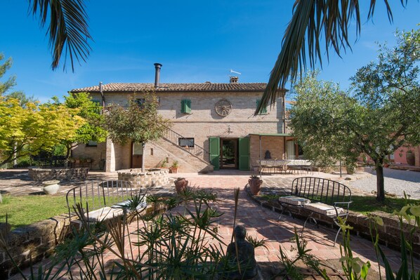 A stone building with a tiled roof, a central staircase, and a courtyard with seating and plants.